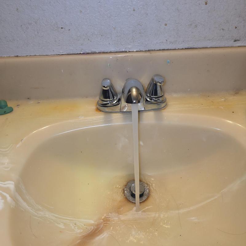 Bathroom faucet with running water and stained sink basin