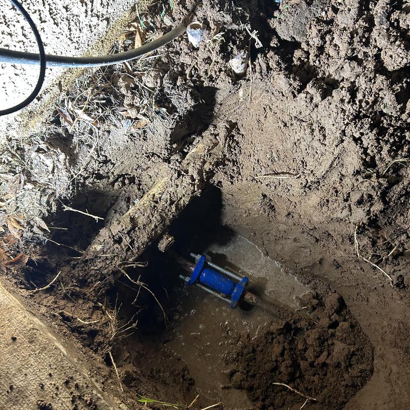 Water main pipe with blue repair fitting in muddy soil