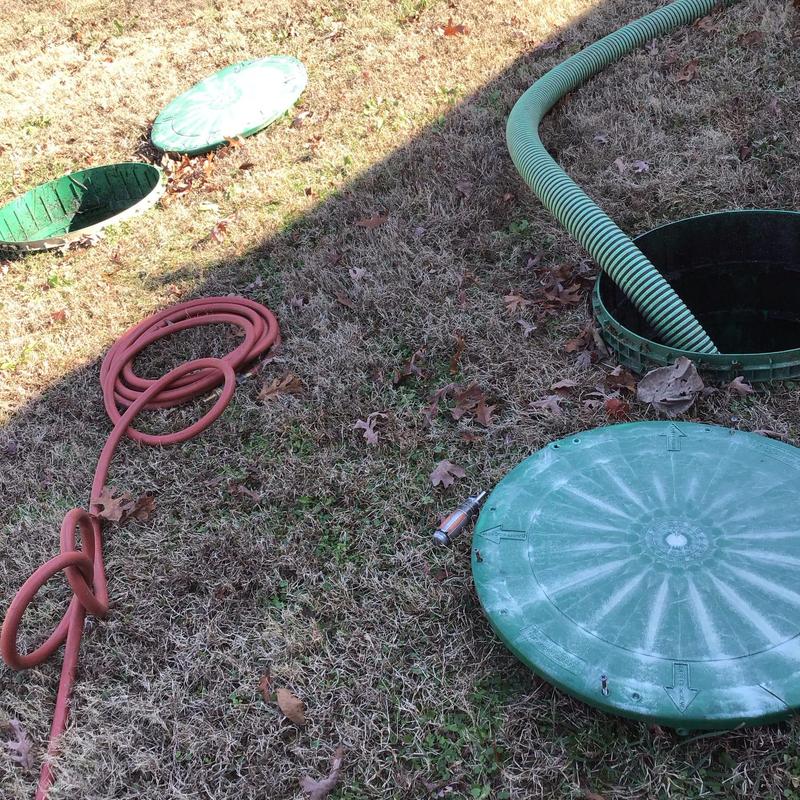 Septic tank risers with pump hose on brown grass