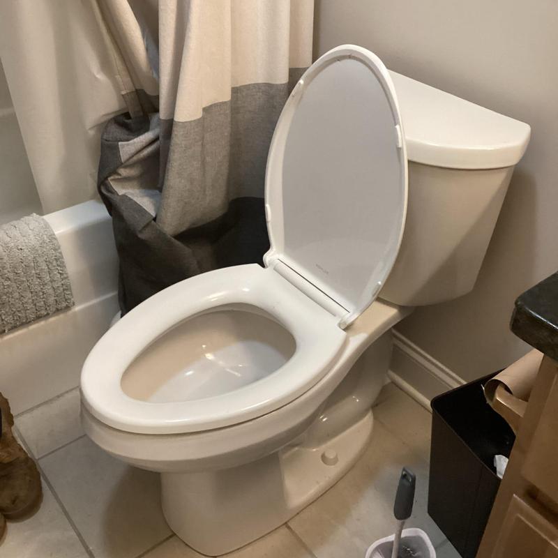 Toilet bowl and tank with open seat in bathroom