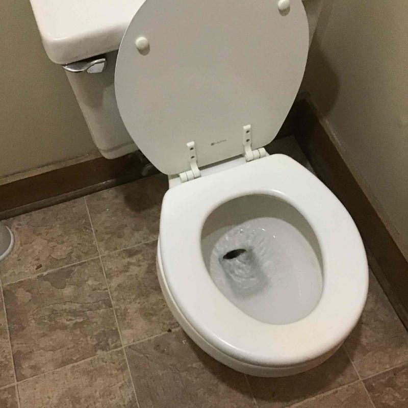 Toilet bowl with flushing water in bathroom corner
