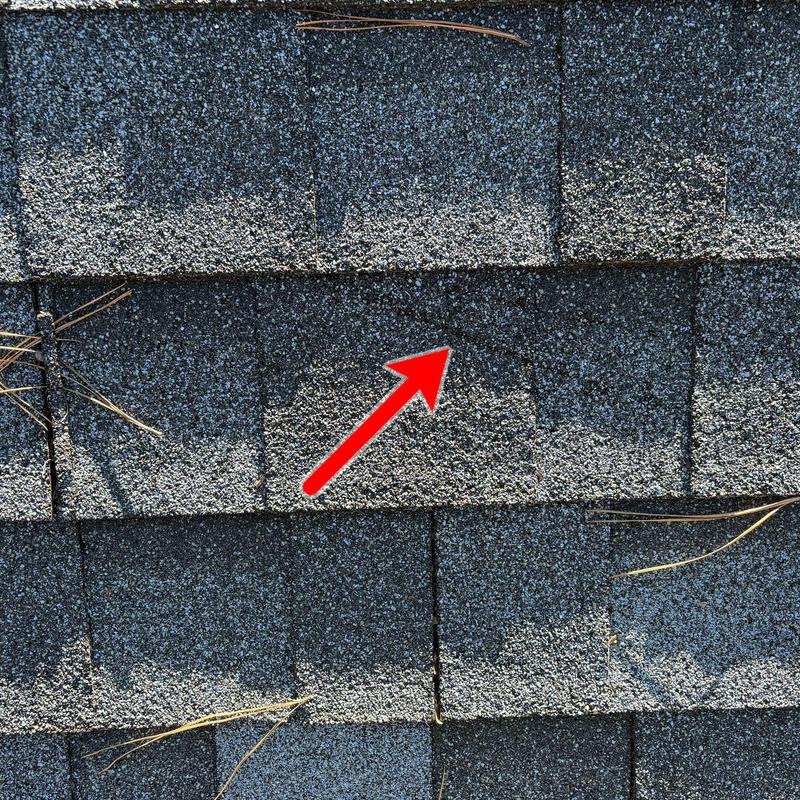 Asphalt roof shingles with hail damage marked by arrow