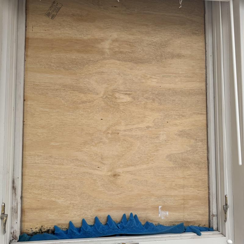 Wood window boarded up with plywood panel and blue fabric
