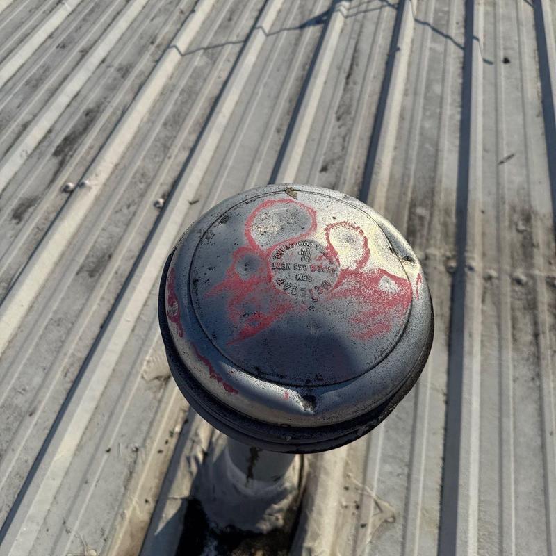 Roof vent cap with visible rust and dents on metal roof