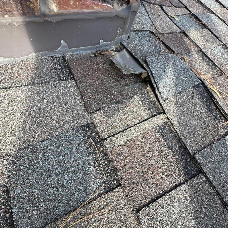 Roof shingles near chimney with lifted edges and damage