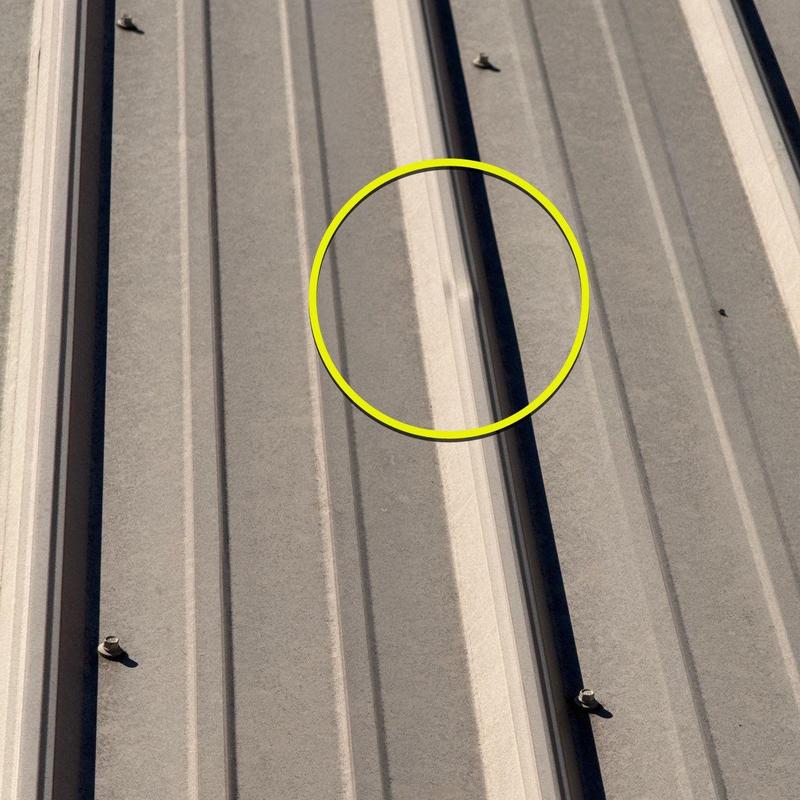 Metal roof panel with dent damage circled in yellow