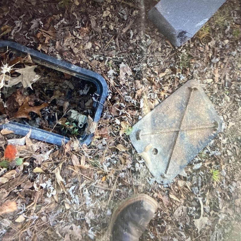 PVC valve box with open lid in leaf-covered ground