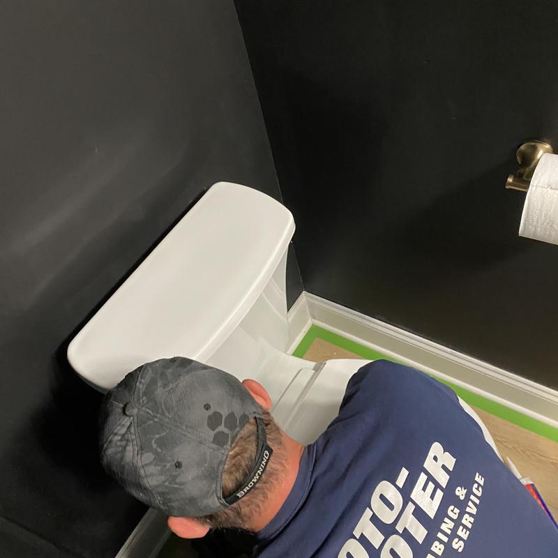 Toilet tank tightening by plumber in bathroom corner
