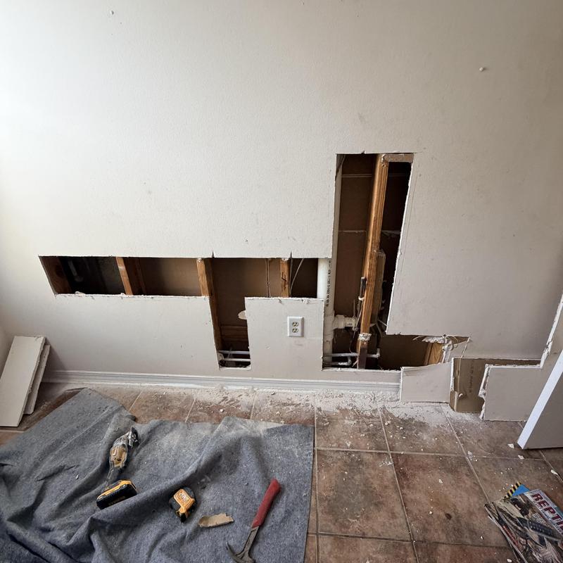 PEX piping installation behind drywall with tools on floor