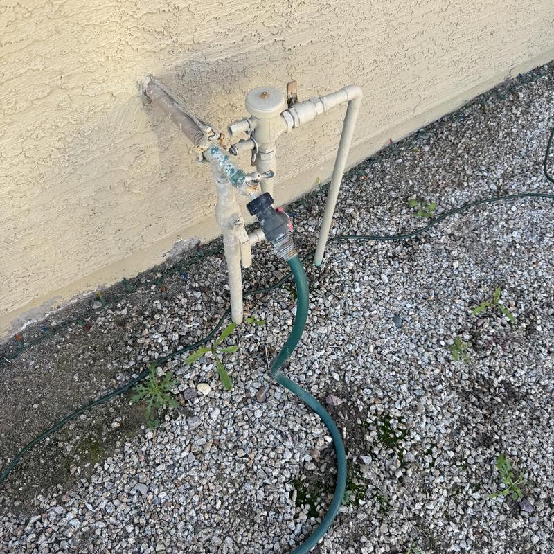 Hose bib with attached garden hose near stucco wall