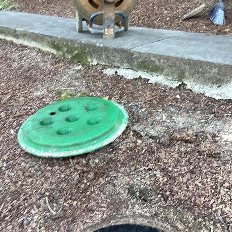 Septic tank lid beside exposed soil near sidewalk