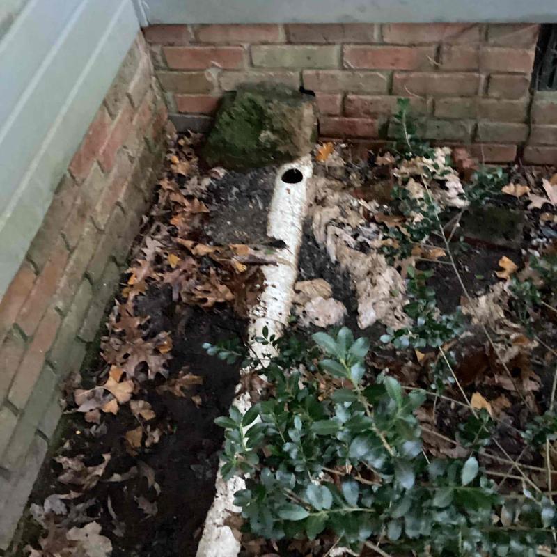 Mainline sewer pipe exposed near brick foundation and cleanout