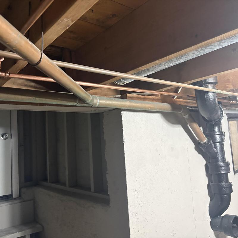 Old copper shower riser and water pipes under floor joists