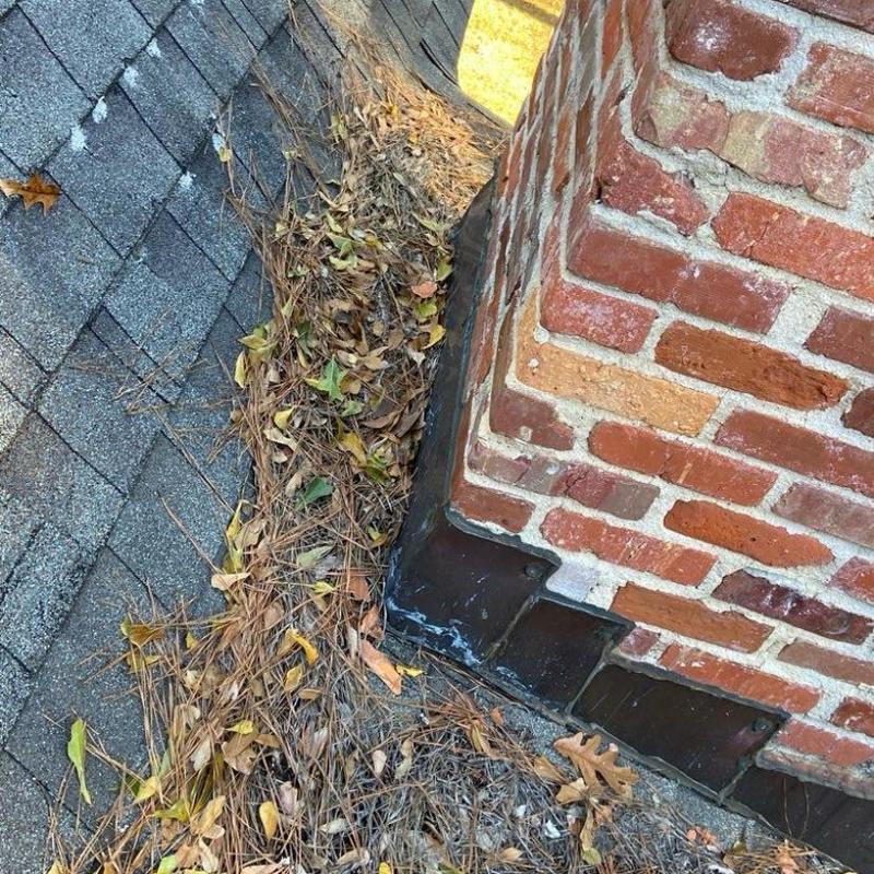 Chimney flashing with leaf debris on asphalt roof shingles Chimney flashing with leaf debris on asphalt roof shingles