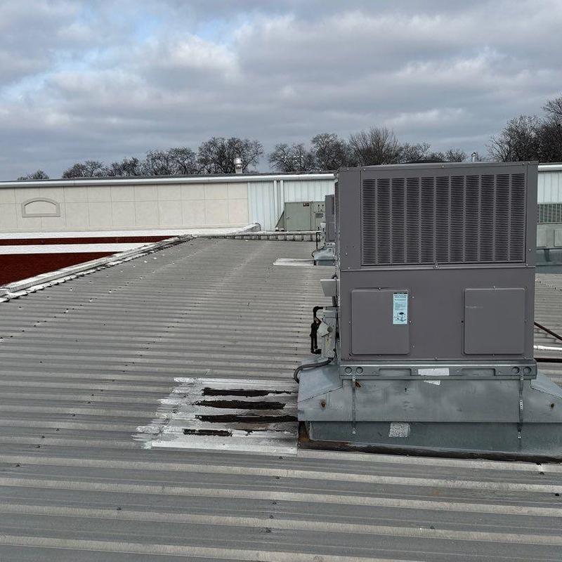 Commercial metal roof with hail damage near HVAC unit