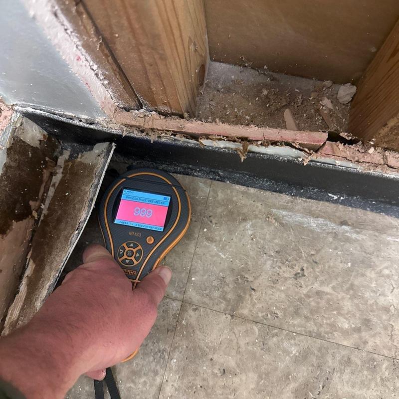 Moisture meter near damaged wall baseboard wood studs