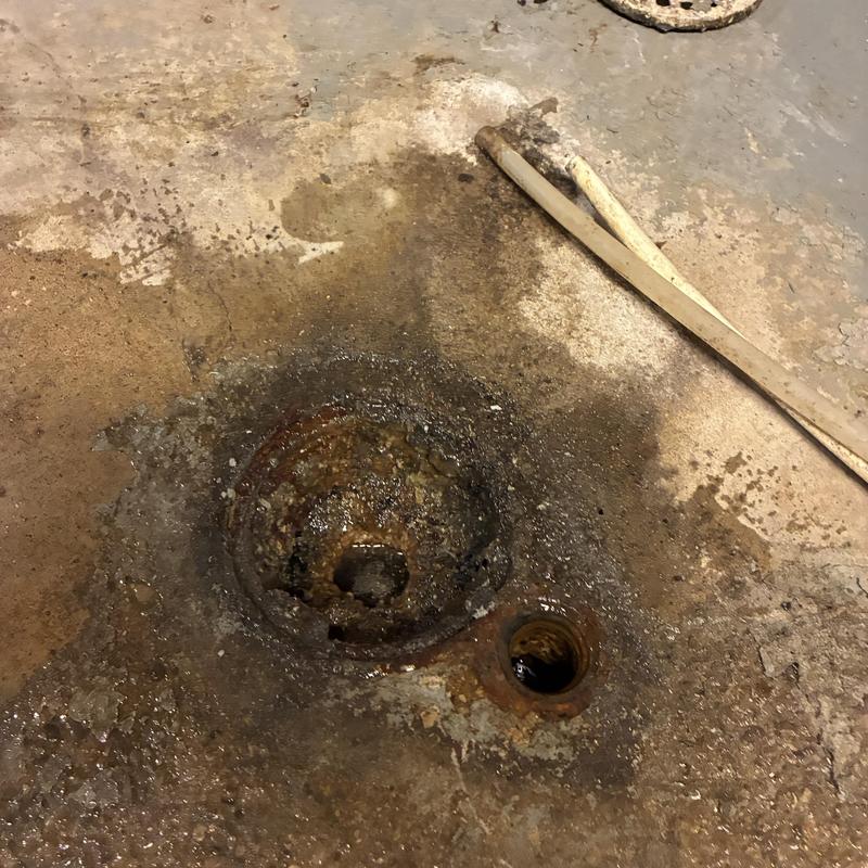 Laundry drain opening with rust and dirt buildup in basement