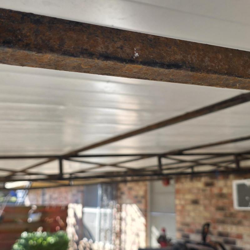 Metal carport frame with rust buildup under roof panels