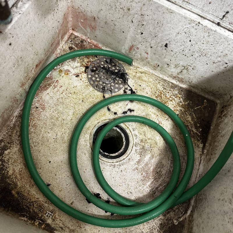 Floor drain clogged with green hose in commercial sink