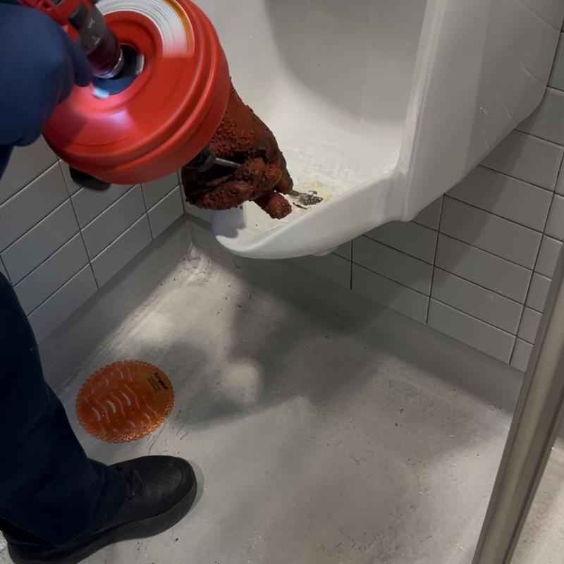 Urinal drain snake clearing clog in restroom