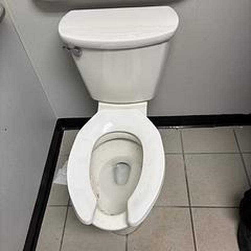 Toilet bowl with open front seat in restroom corner