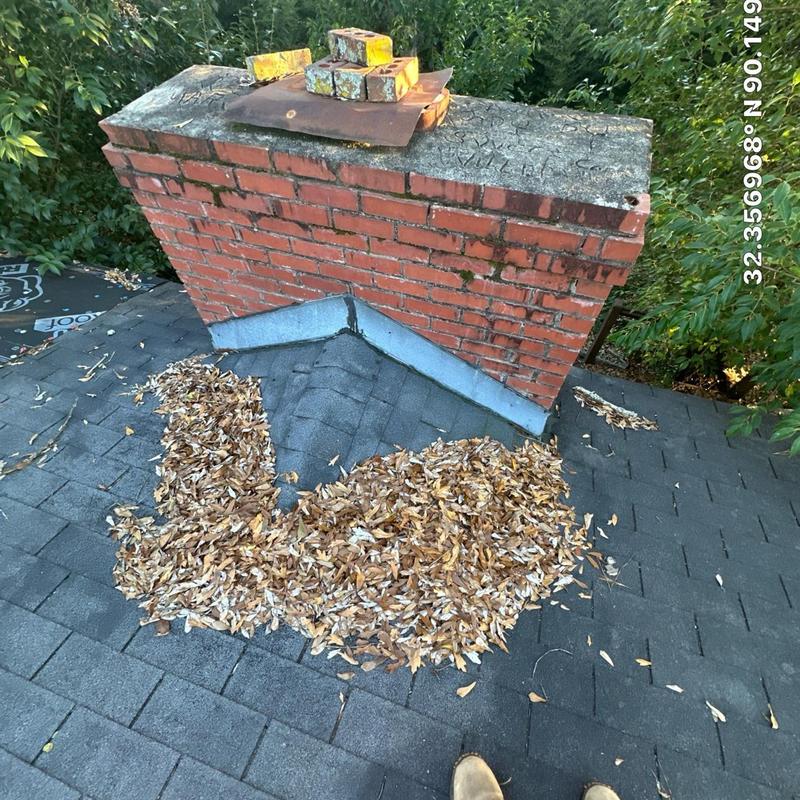 Brick chimney flashing with debris on asphalt roof