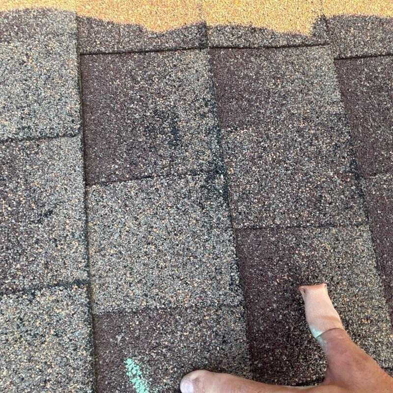 Asphalt roof shingles with damage marks and hand pointing