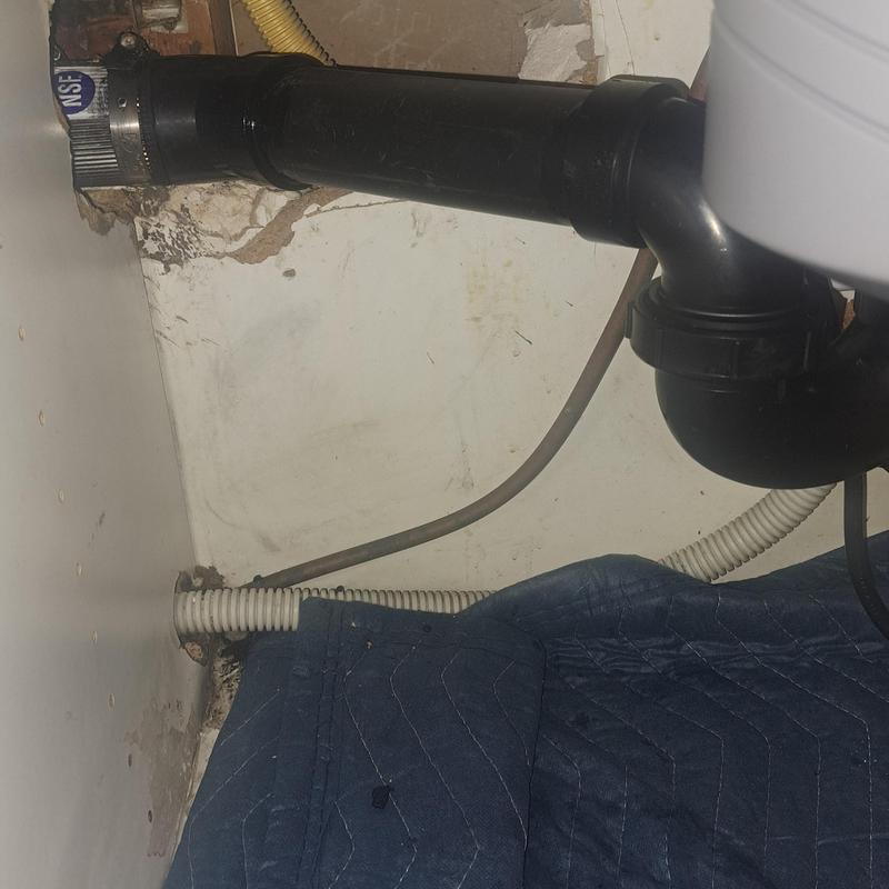 Black kitchen drain pipe under sink with wall damage Black kitchen drain pipe under sink with wall damage