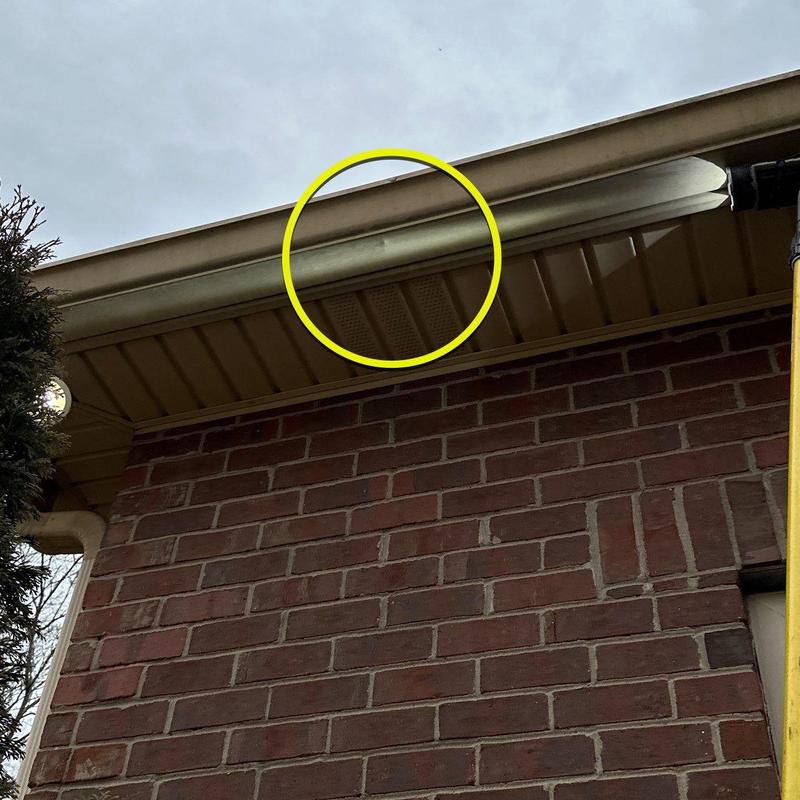 Gutter with dented section circled in yellow on brick house