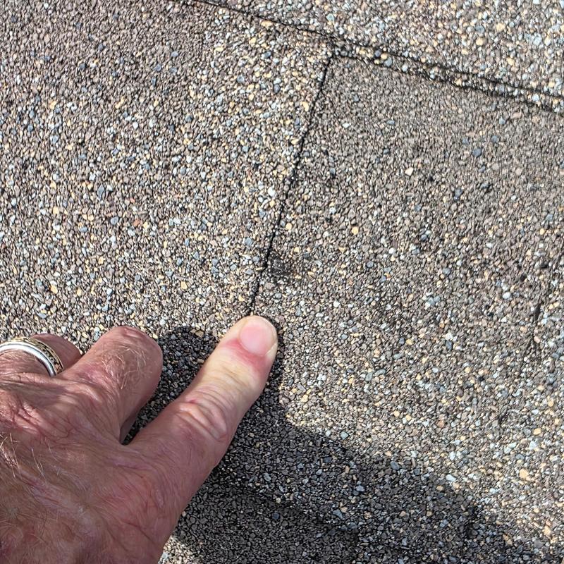 Roof shingles showing hail damage close-up with finger pointing