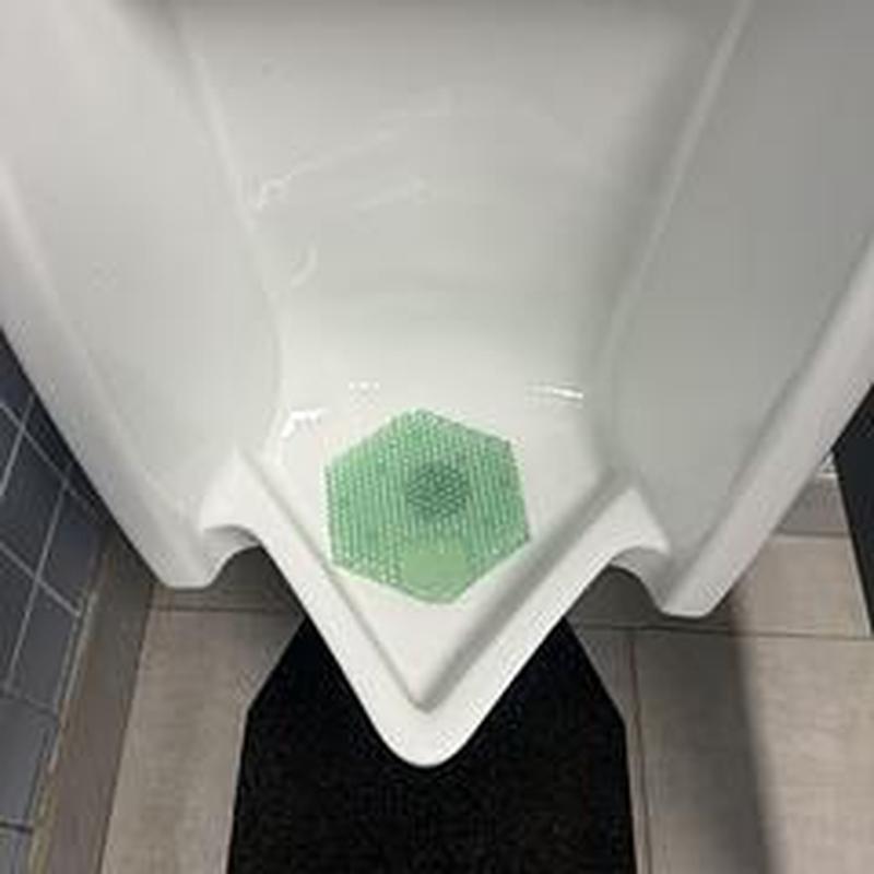 Urinal drain with green splash guard in bathroom stall