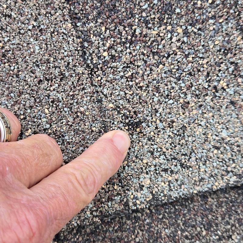 Asphalt shingle with finger pointing at potential leak area