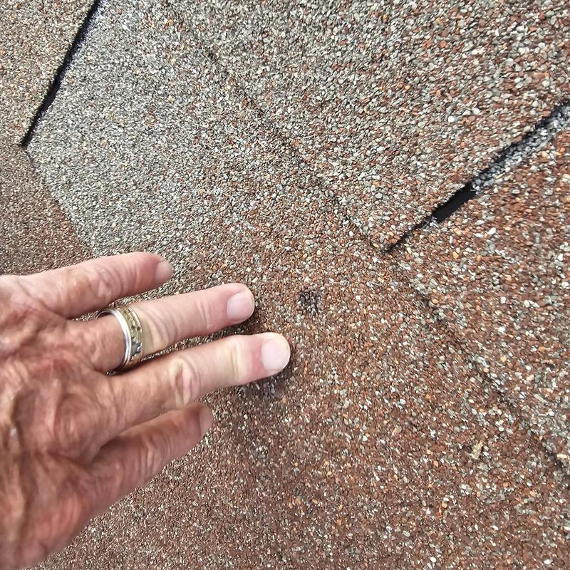 Asphalt shingle roof hail damage close-up with hand
