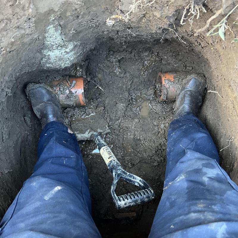 Sewer pipe exposed with shovel and work boots in dirt
