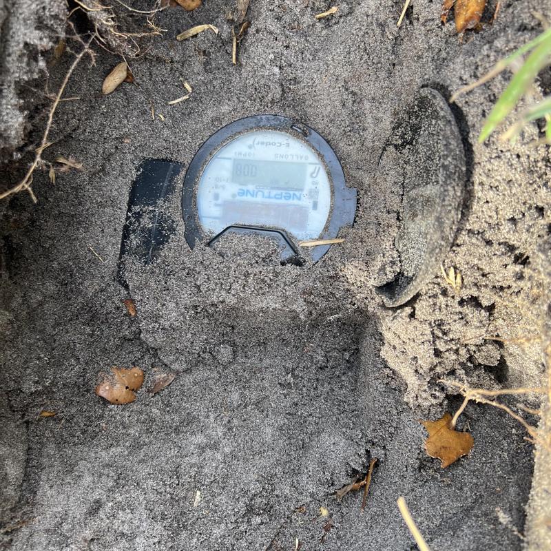 Water meter partially buried in sand with open cover