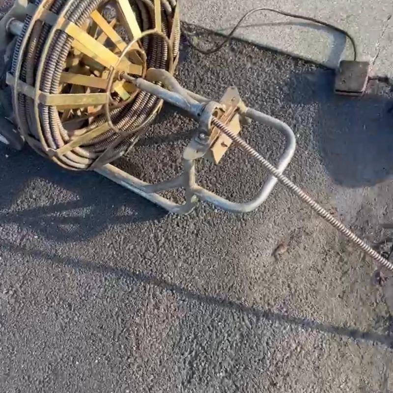 Drain snake machine clearing main drain clog on pavement