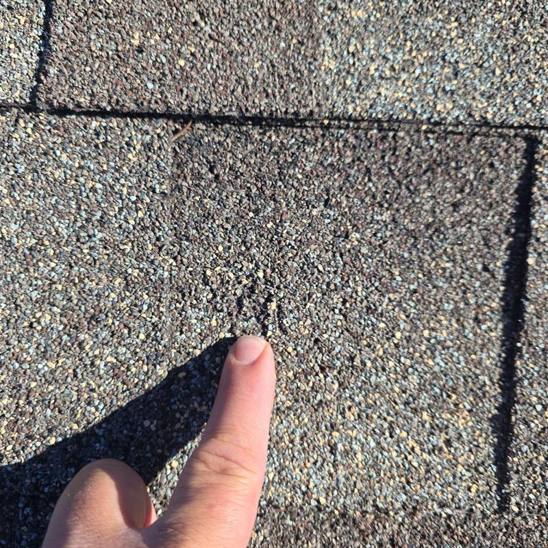 Asphalt shingle roof with hail damage close-up and finger