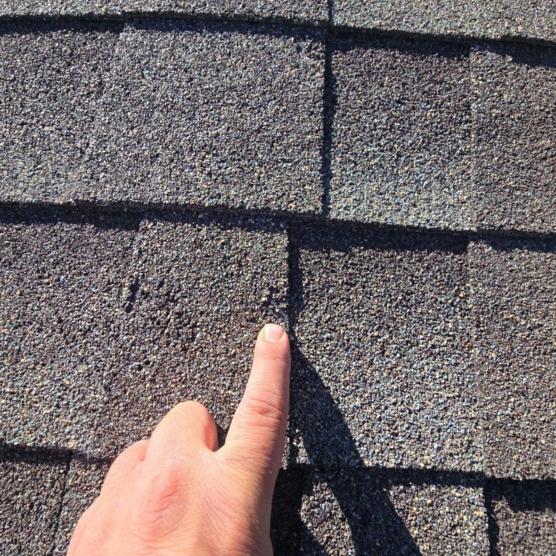 Shingle roof hail damage close-up with finger pointing