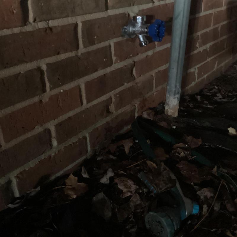 Hose bib with blue handle installed on brick wall