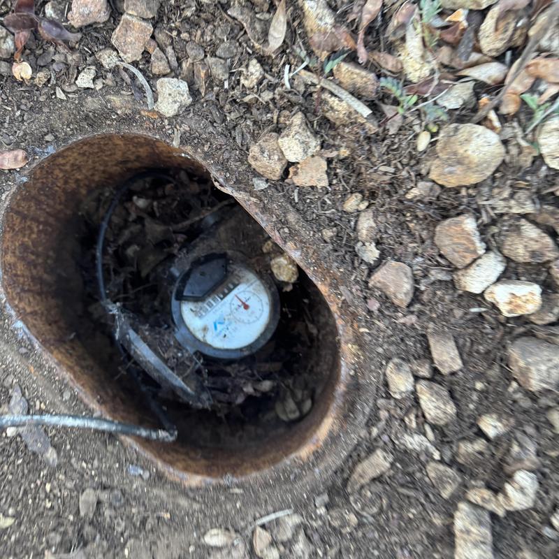 Water meter in ground pit with dirt and rocks