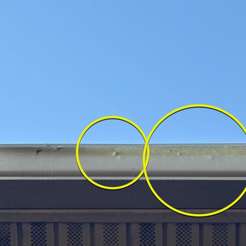 Metal gutter dents from hail damage highlighted