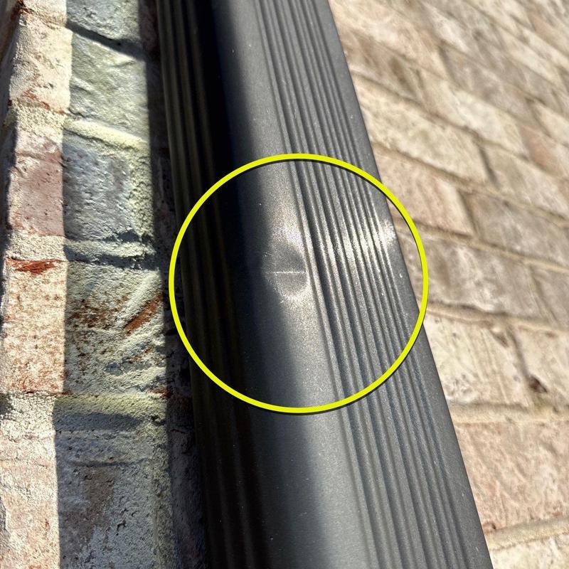 Aluminum downspout with dent damage on exterior wall