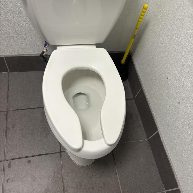 Commercial toilet with open front seat in restroom corner