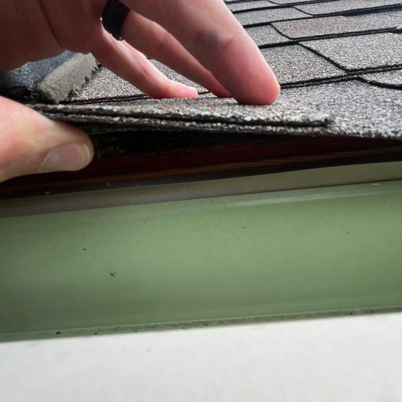 Asphalt shingles lifting on roof edge revealing damage