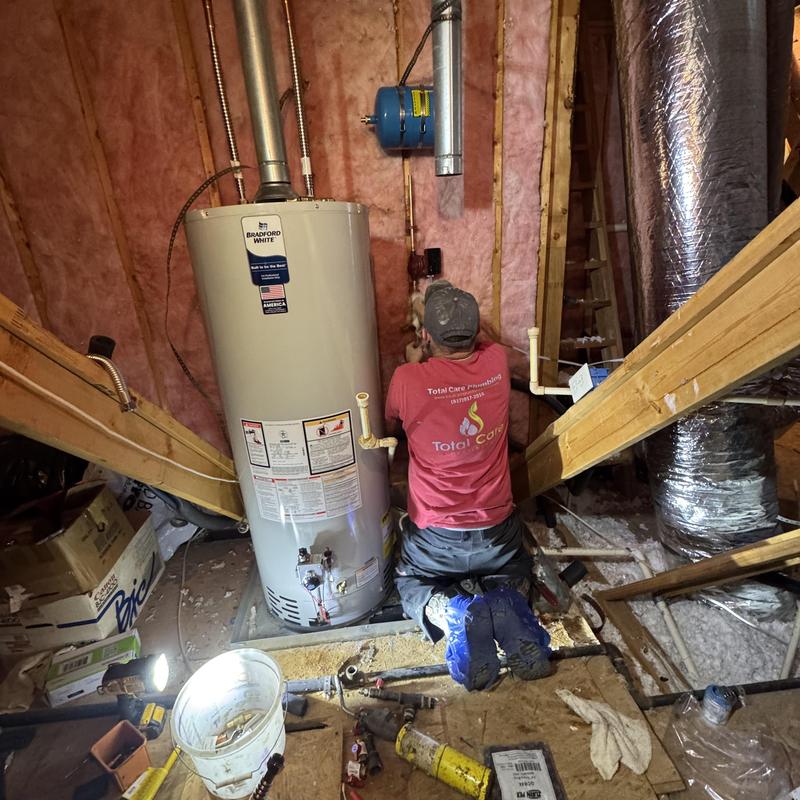 Water heater installation in attic with plumber kneeling