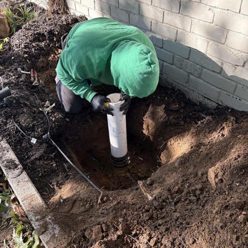 PVC sewer pipe installation in dug hole near brick wall