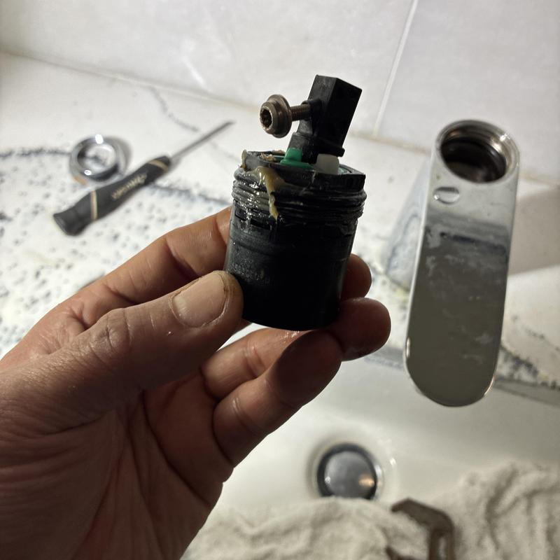 Faucet cartridge held by hand near sink and tools