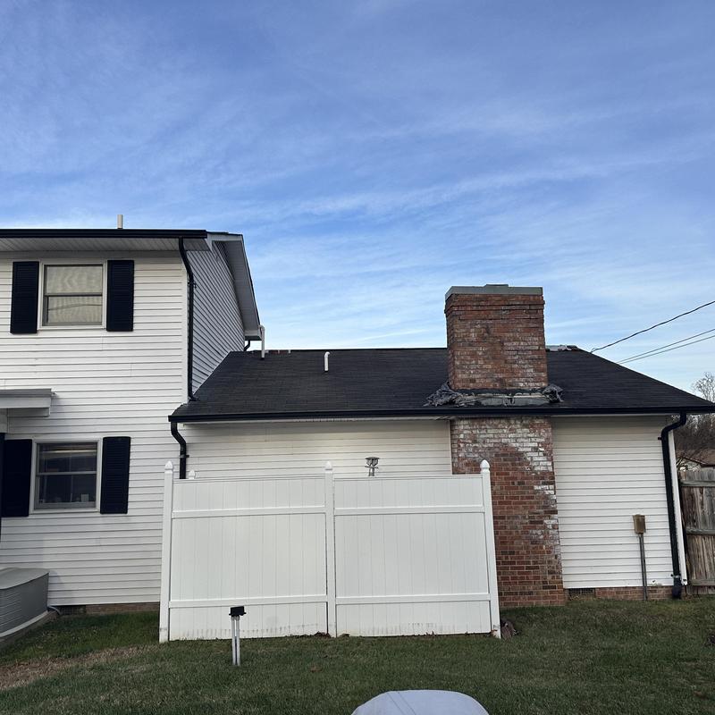 Black roof with brick chimney on white home