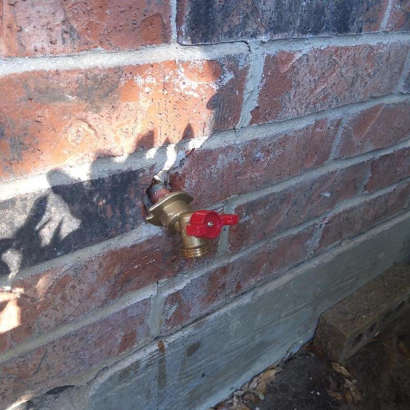 Hose spigot with red handle mounted on brick wall