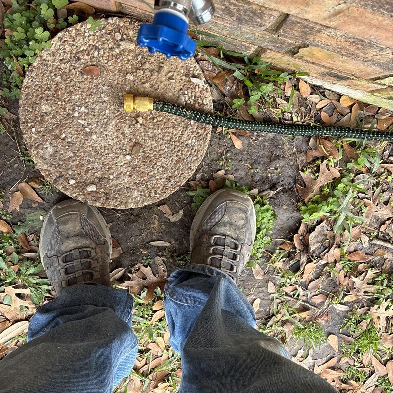 Hose bib with green garden hose and worker shoes